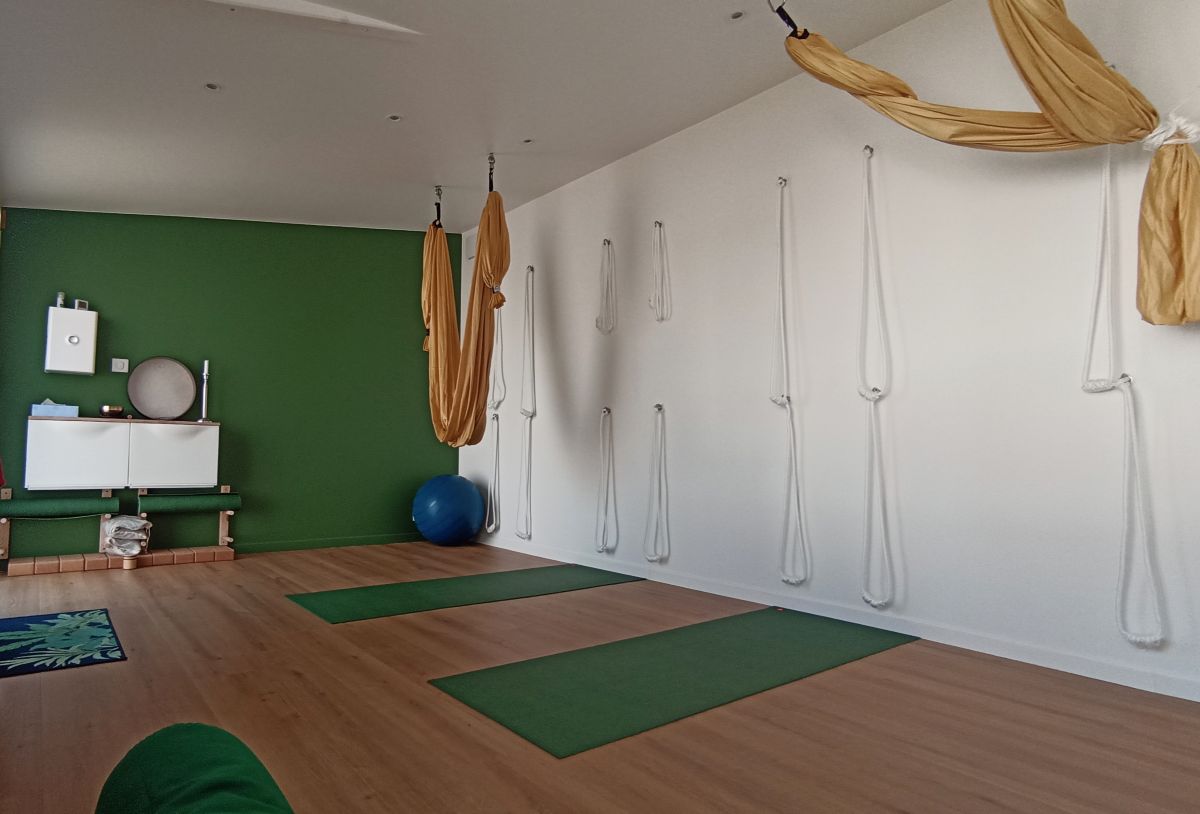 Intérieur du studio Yodéga : mur vert sapin, parquet bois et hamacs de yoga aérien dorés